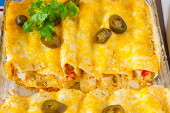 Creamy White Sauce and Crab Enchiladas in a baking dish topped with cheddar cheese and jalapenos