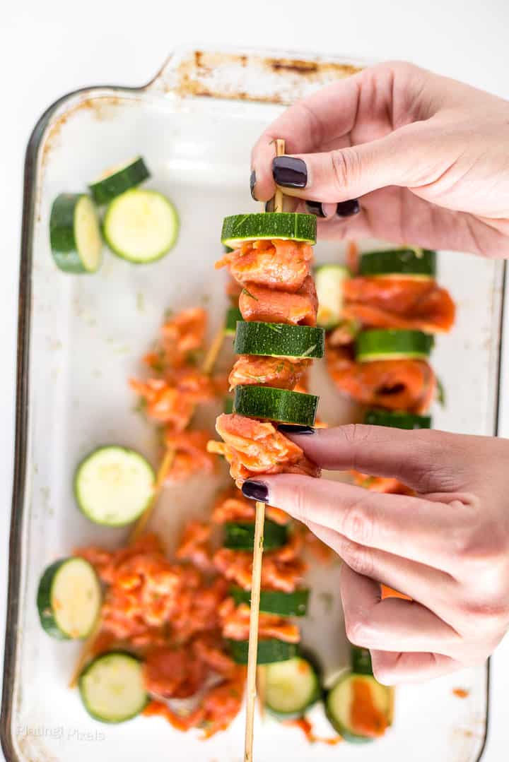 Process shot showing someone placing salmon piece on a skewer to make kabobs
