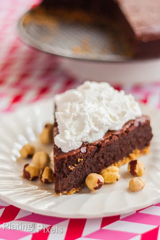 A close up of Chocolate Hazelnut Fudge Cake on a plate with whipped cream