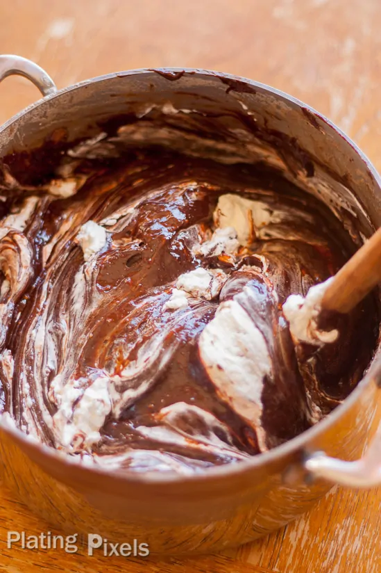 Process shot of mixing Chocolate Fudge Cake batter in a large mixing bowl with a wooden spoon