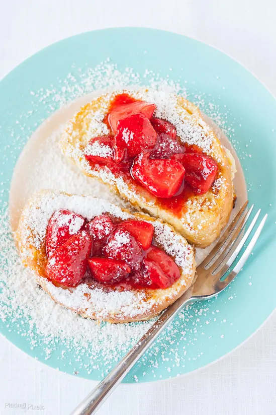 Two Banana Cream Cheese Stuffed French Toast with Strawberry Topping on a plate sprinkled with powdered sugar