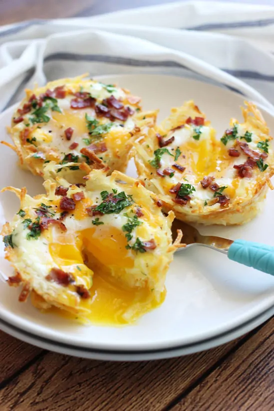 Three just baked Hash Brown Egg Nests on a plate. One with egg yolk running out of it.