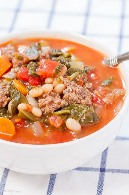 A side shot of tomato basil beef stew in a bowl with beans and veggies