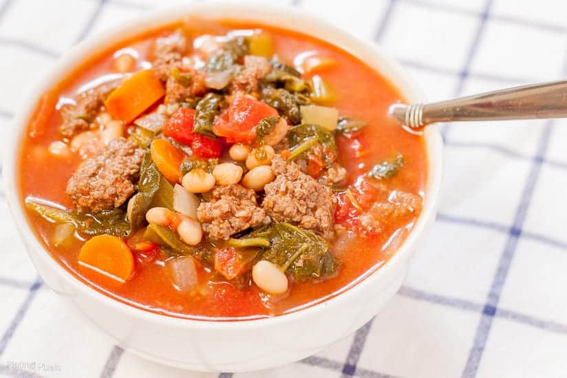 A close up of a bowl of tomato beef stew sitting on a checked tablecloth