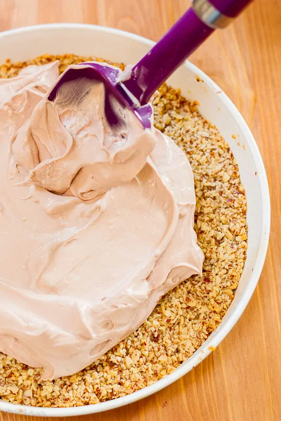 Spreading chocolate pudding cheesecake mix over almond crust in a spring-form pan