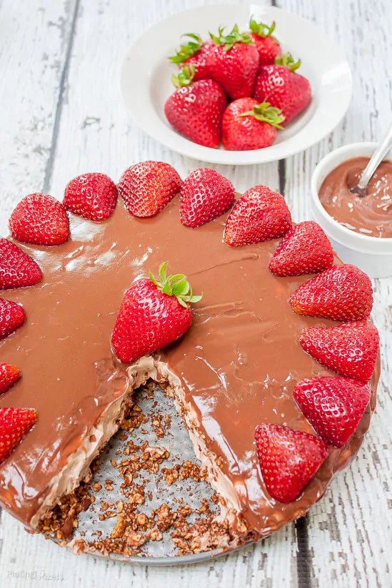 No Bake Chocolate Pudding Cheesecake topped with strawberries on a white table with slice cut out