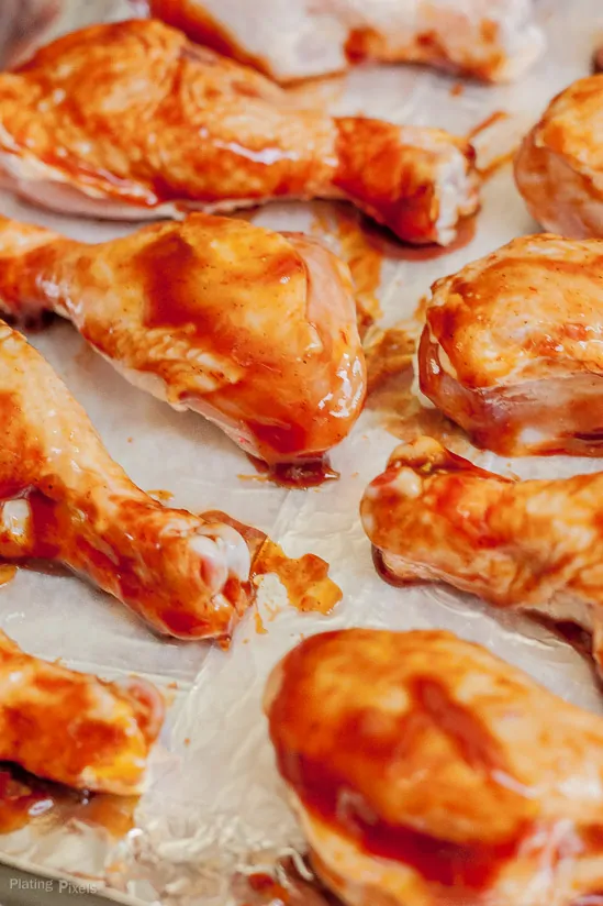 BBQ sauce smothered chicken drumsticks on a baking tray before going in the oven to bake