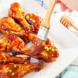 Brushing barbecue sauce over Oven Baked Honey BBQ Chicken Drumstick on white plate
