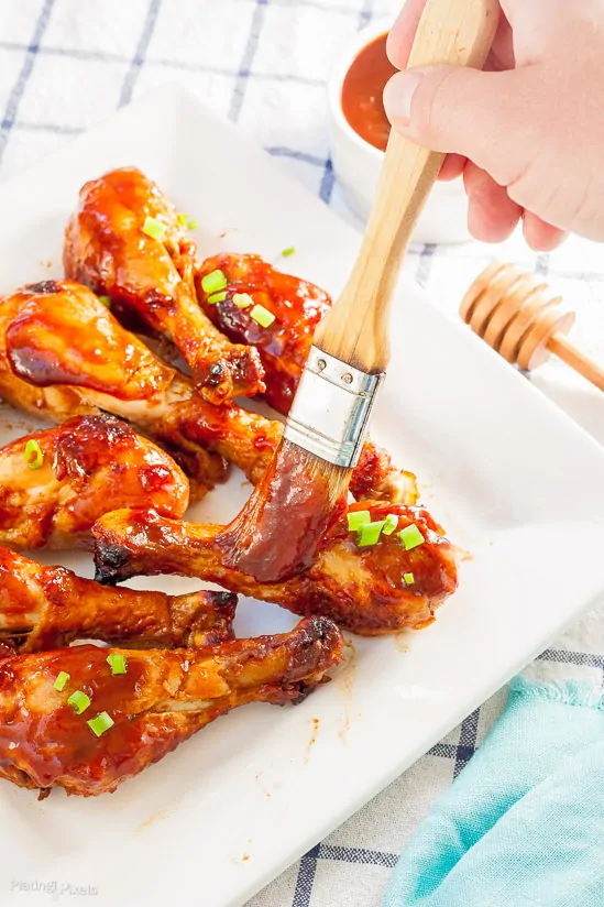 Process shot of hand brushing a bbq glaze over Easy Honey BBQ Oven Baked Chicken Drumsticks