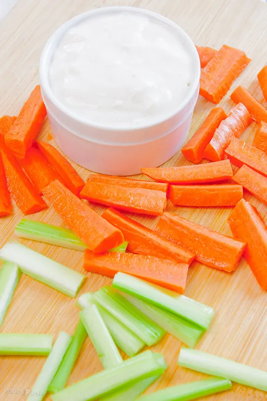 Blue cheese dressing for dipping with carrot and celery sticks on a cutting board