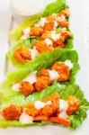 Four Buffalo Chicken Lettuce Wraps drizzled with blue cheese dressing on a white plate