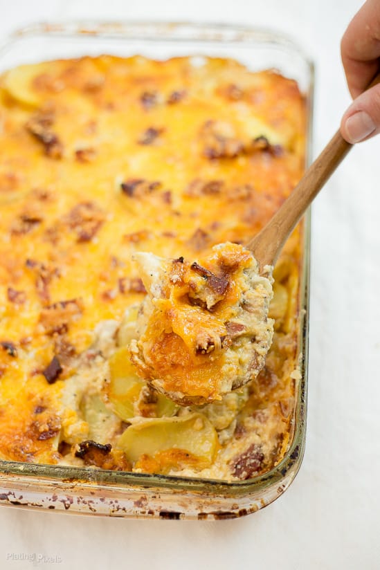 Candied Bacon Au Gratin Potatoes in a large dish being scooped with wooden serving spoon