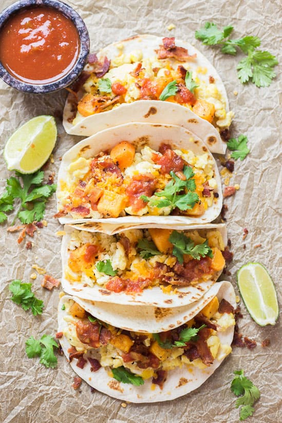 An overhead shot of four Sweet Potato Breakfast Tacos garnished with lime wedges and cilantro