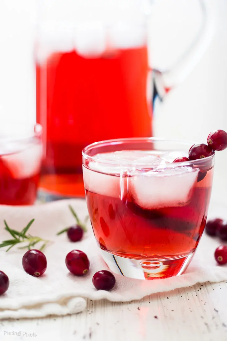An Apple Cranberry Ginger Ale Spritzer in a glass with fresh cranberries scattered around