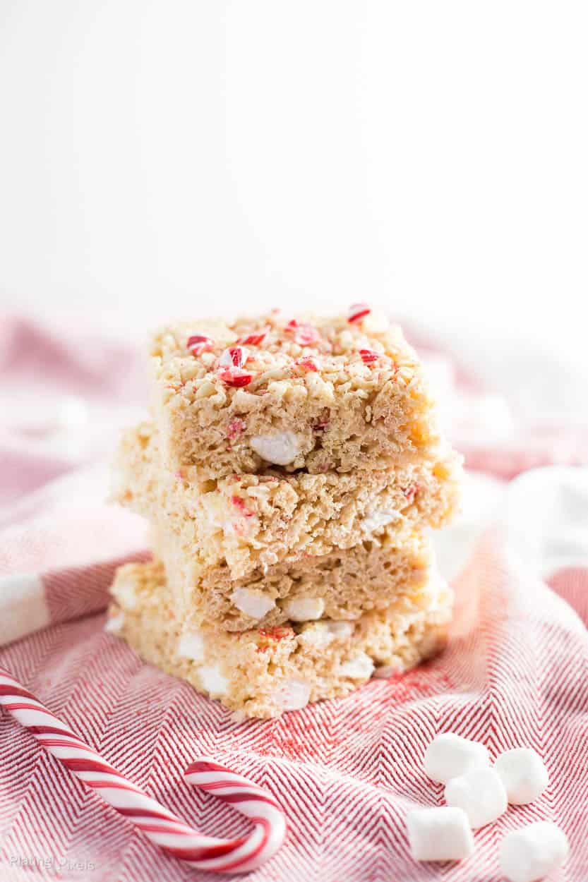 A close up of a stack of Brown Butter Peppermint Rice Krispie Treats with candy canes scattered around