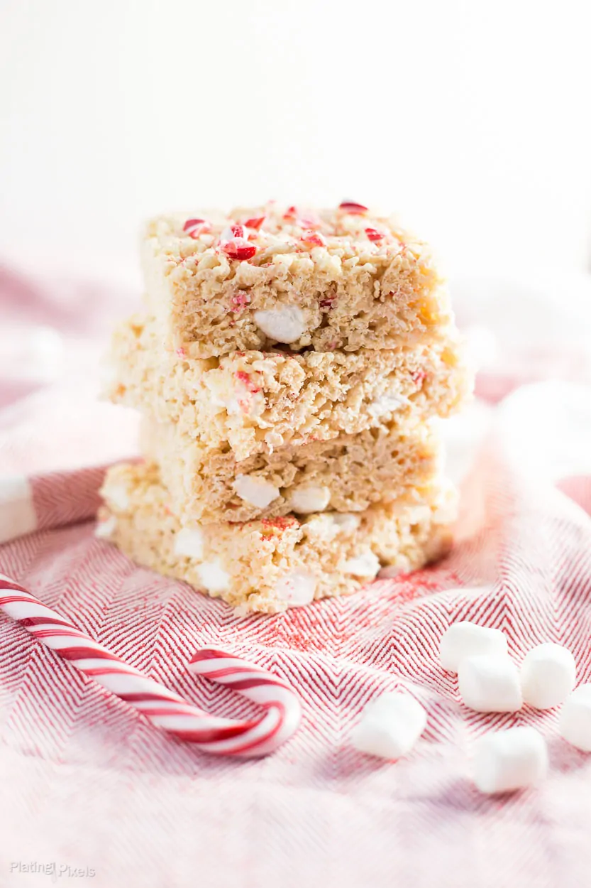 A close up of Brown Butter Peppermint Rice Krispie Treats stacked on top of each other with candy canes crushed on top