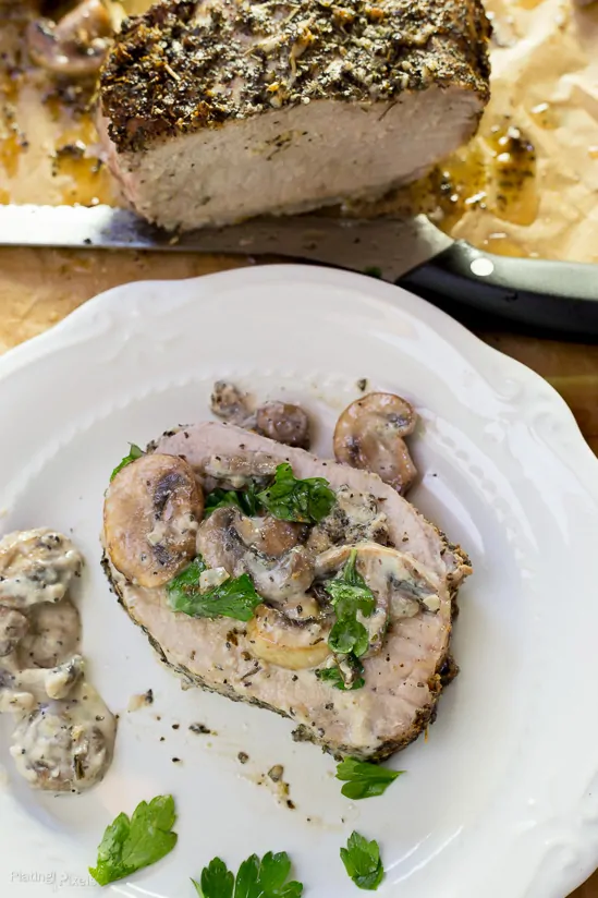 A slice of Garlic Herbed Pork Loin on a plate with Mushroom Wine Sauce over the top