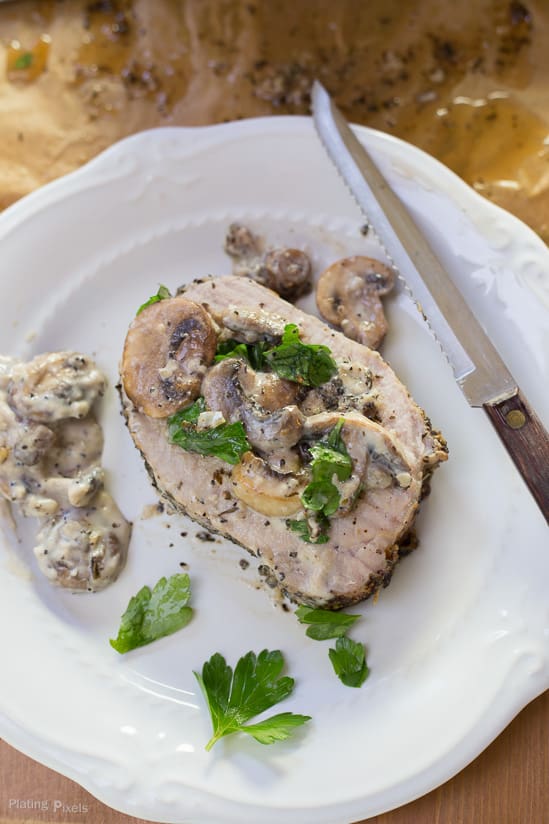 A close up of a slice of Garlic Herbed Pork Loin on a white plate with Mushroom Wine Sauce on top