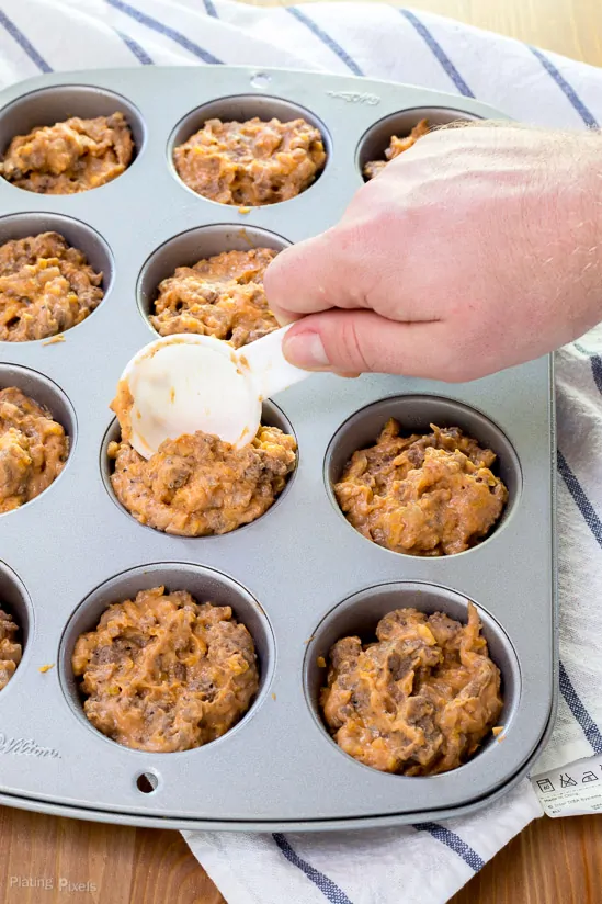 A hand scooping some Mini Cheeseburger Muffins batter into a muffin pan