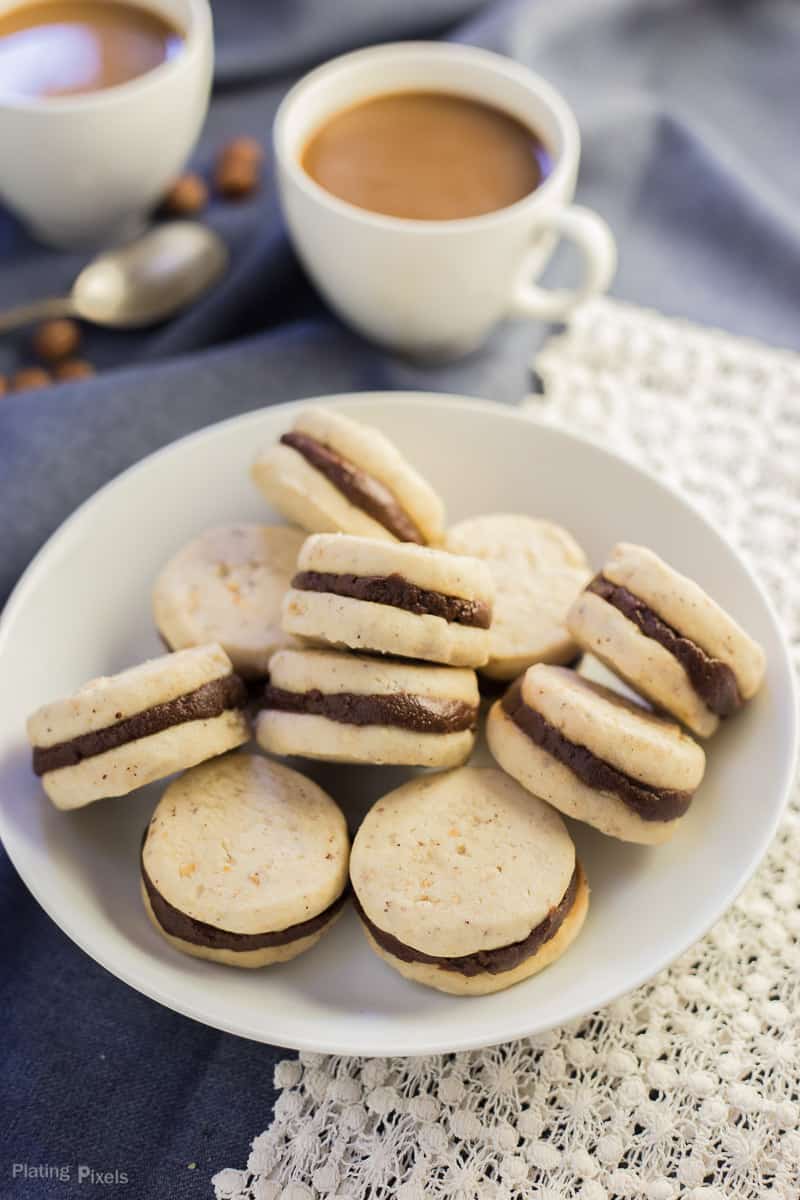 Pumpkin Spice Chocolate Filled Shortbread Cookies on a plate with two cups of coffee in background