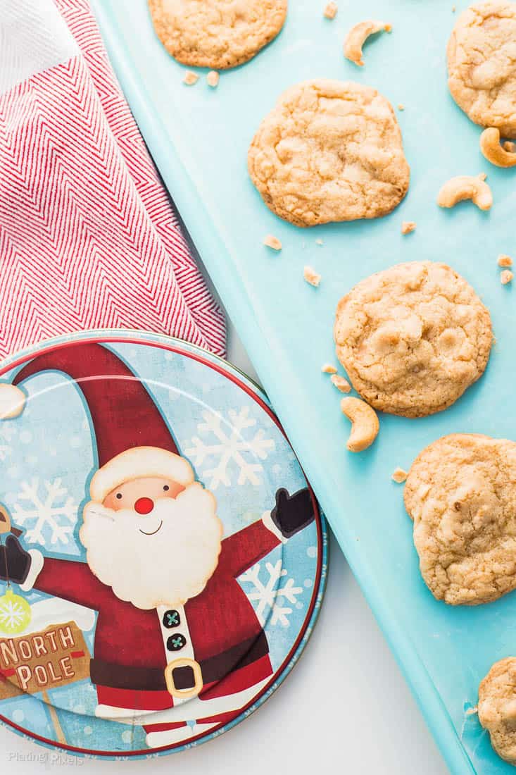 A close up of Chewy Cashew Toffee Cookies on a baking sheet with a Santa themed cookie tin beside it