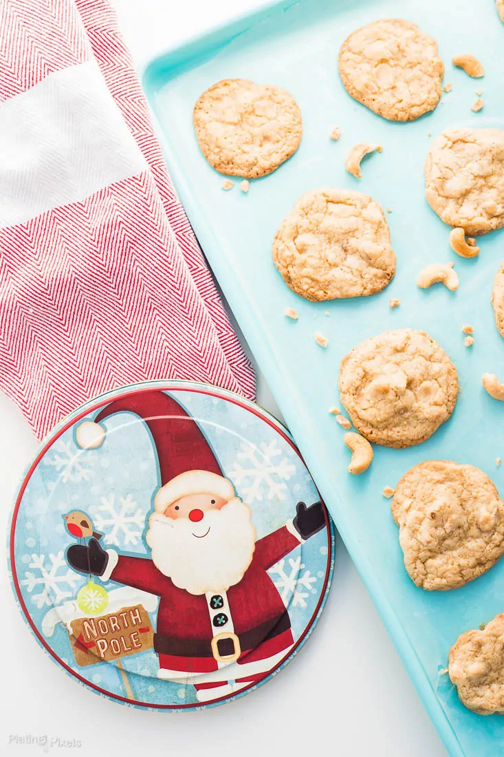 Chewy Cashew Toffee Cookies on teal cookie sheet with a santa decorated cookie tin beside it
