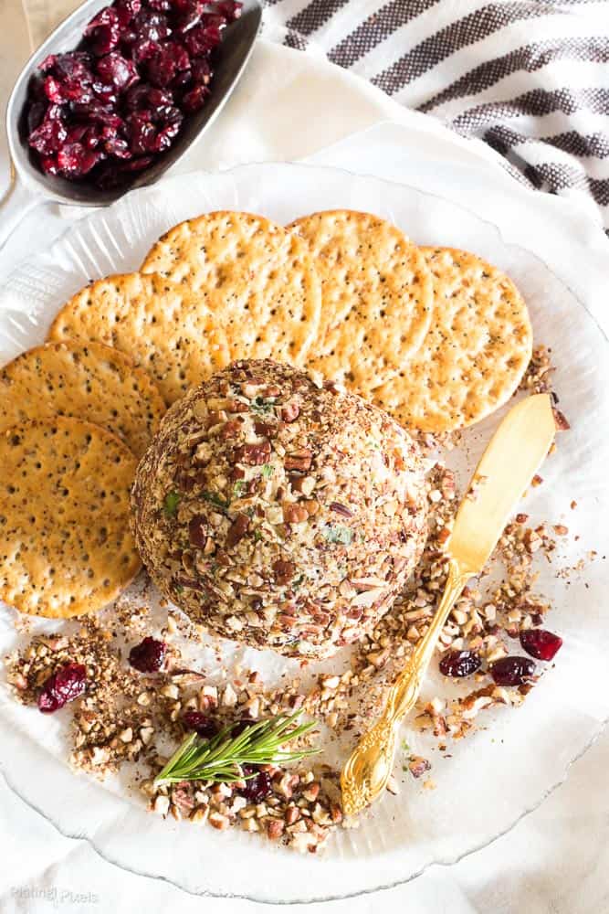 An overhead shot of Craisins White Cheddar Cheese Ball on a plate with crackers and Craisins as garnish