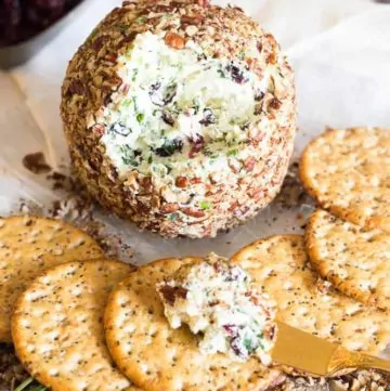 Craisins Cheddar Cheese Ball with scoop taken out of it on a plate next to crackers