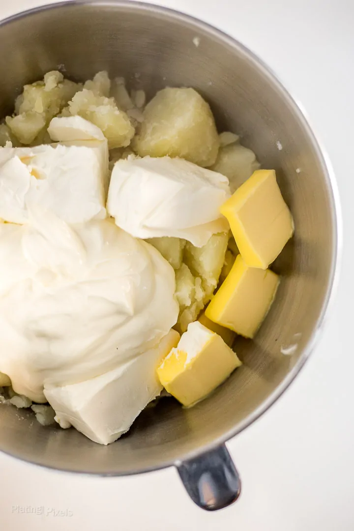 Potatoes, sour cream, butter, cream cheese and milk in a metal mixing bowl