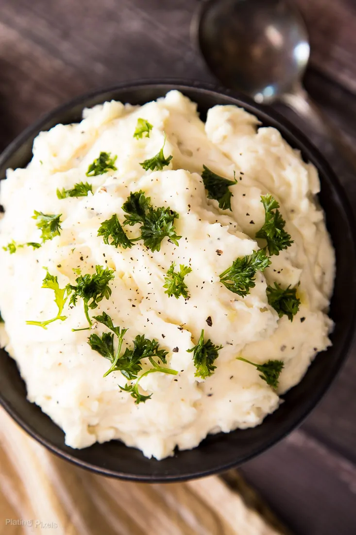 A close up of Creamy Mashed Potatoes in a black bowl garnished with parsley