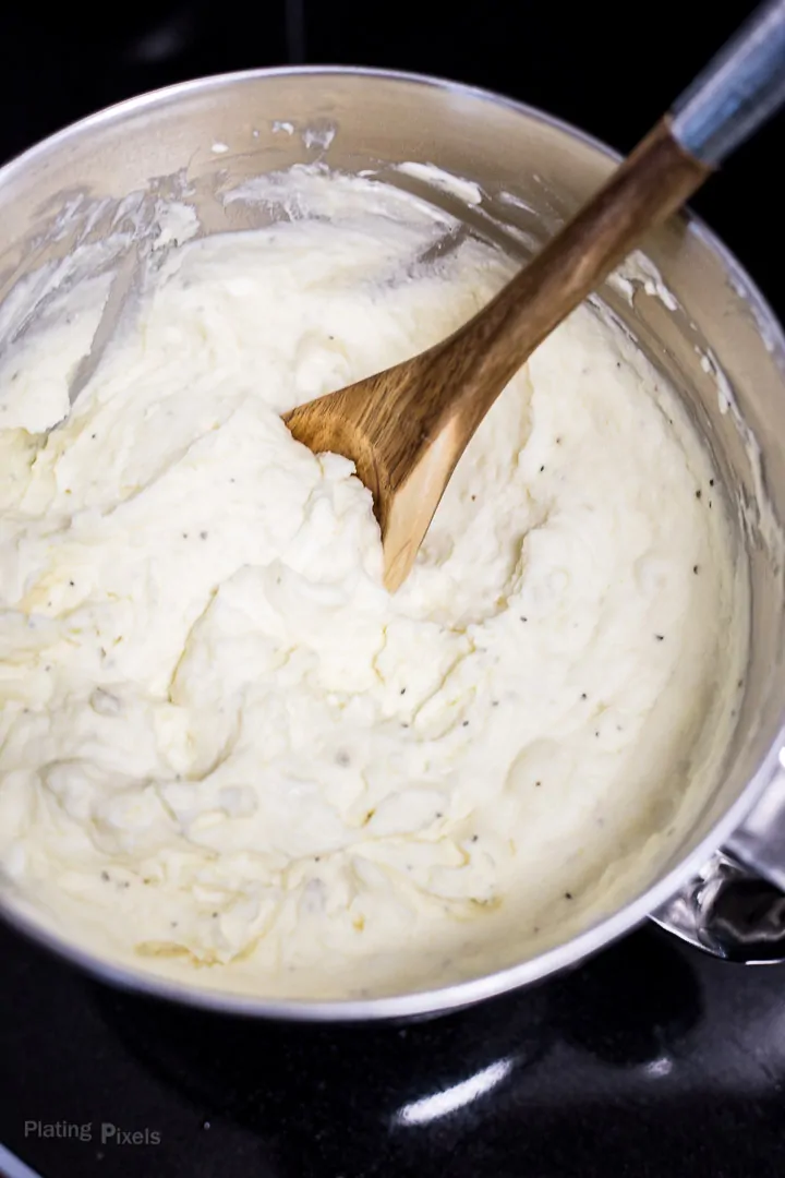 Stirring Creamy Mashed Potatoes in a large metal bowl with a wooden spoon