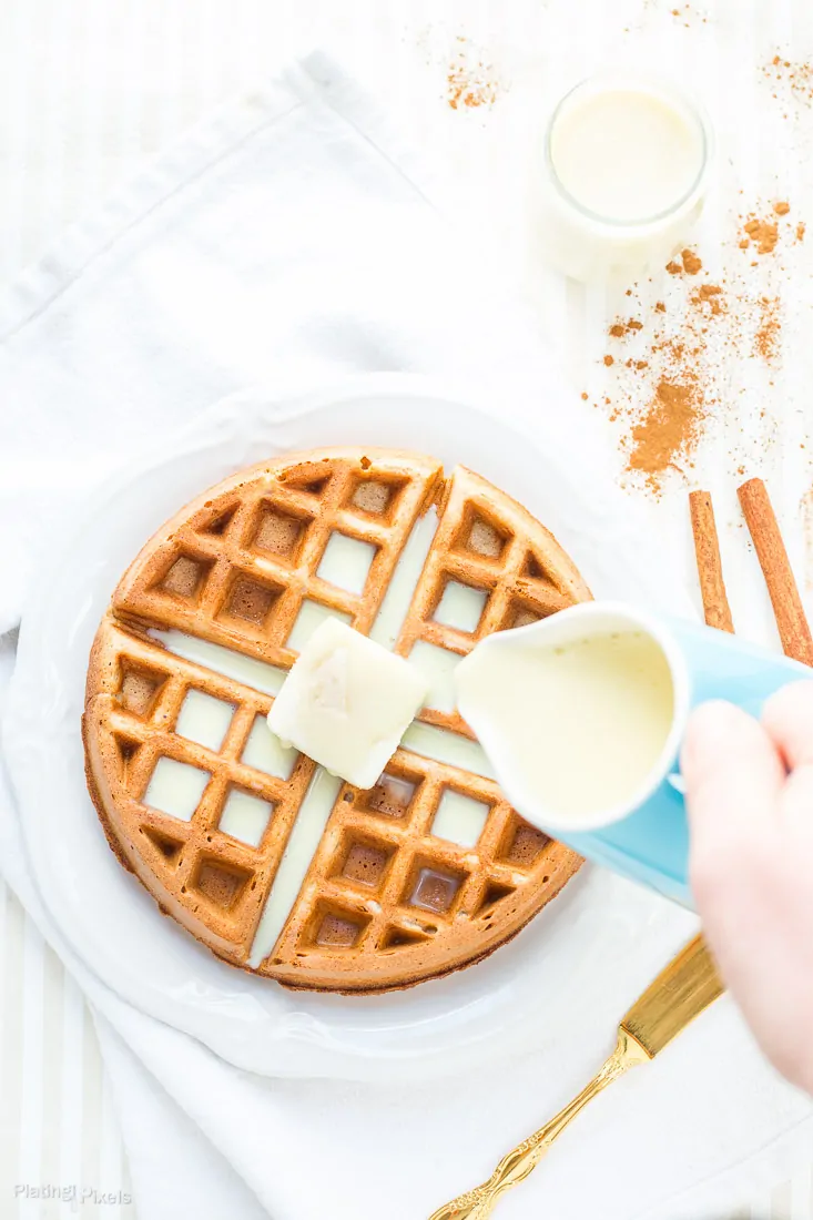 Overhead shot of gluten-free Eggnog Waffles on a plate with hand pouring eggnog drizzle over them