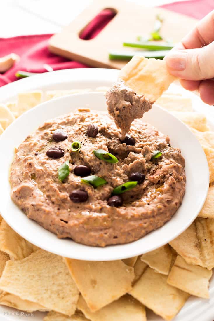 Someone dunking a chip into some sun dried tomato and Black Bean Hummus