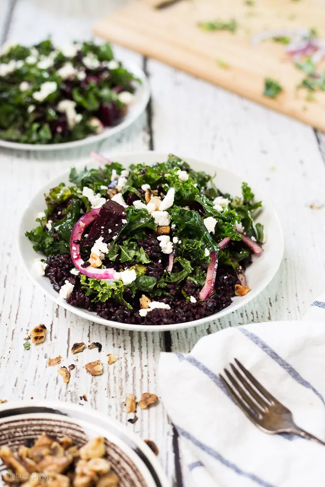 A black rice, kale and beet salad sitting on a white wooden surface
