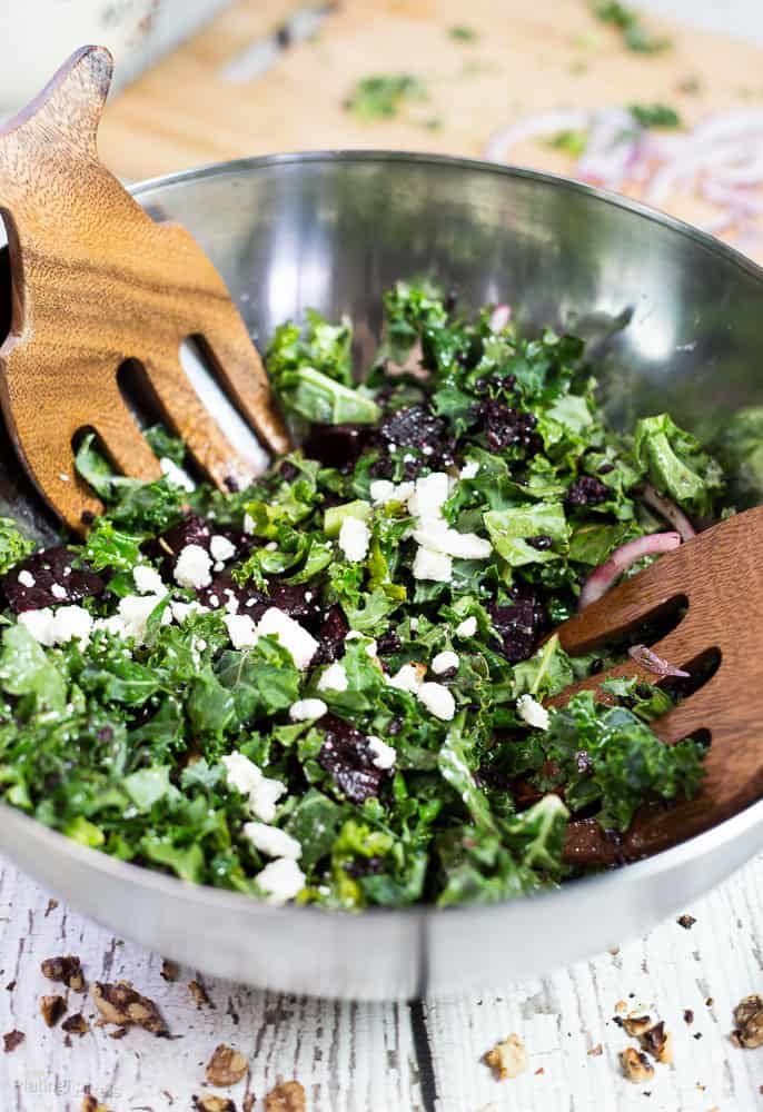 A kale and roasted beet salad in a large bowl with salad servers