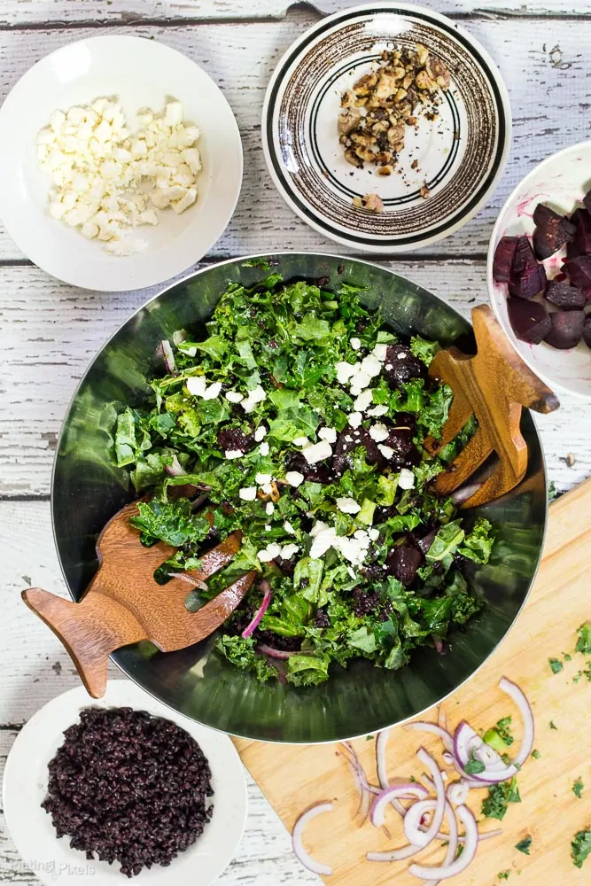 A roasted beet and kale salad in a large serving bowl with ingredients all around it