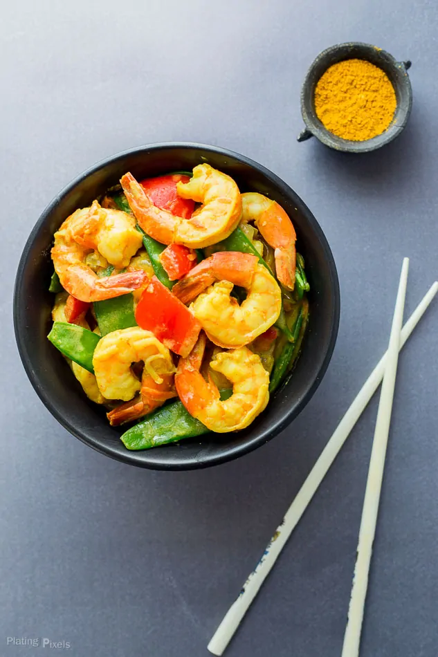 An overhead shot of prepared Coconut Curry Shrimp in a black bowl with veggies next to chop sticks