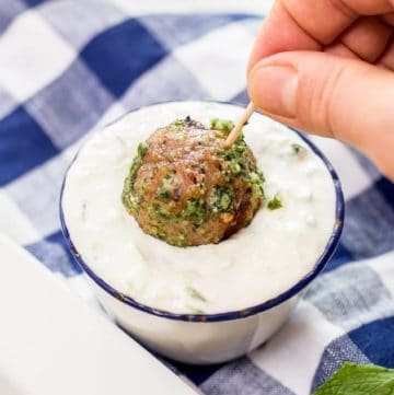 Hand dipping a Greek Turkey Meatball on a toothpick into bowl of Cucumber Mint Sauce