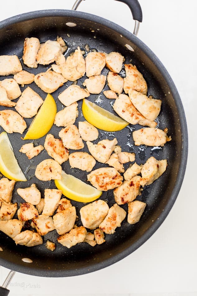 Process shot of chicken browning in a pan with lemon wedges