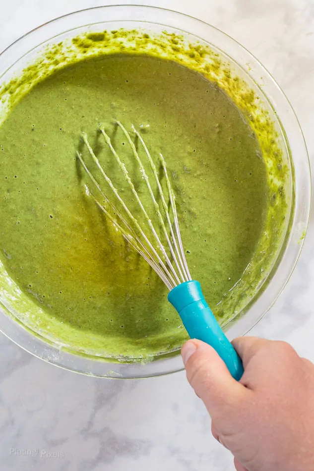 Process shot of stirring Matcha Green Tea Waffle batter in a glass bowl with a whisk