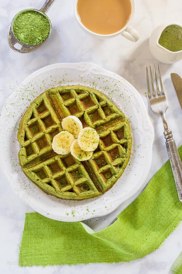 An overhead shot of Matcha Green Tea Waffles on a plate with matcha powder at the side