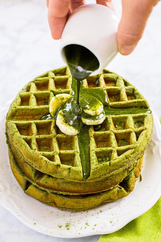 Matcha Green Tea Waffles stacked on a plate with matcha syrup getting poured over the top