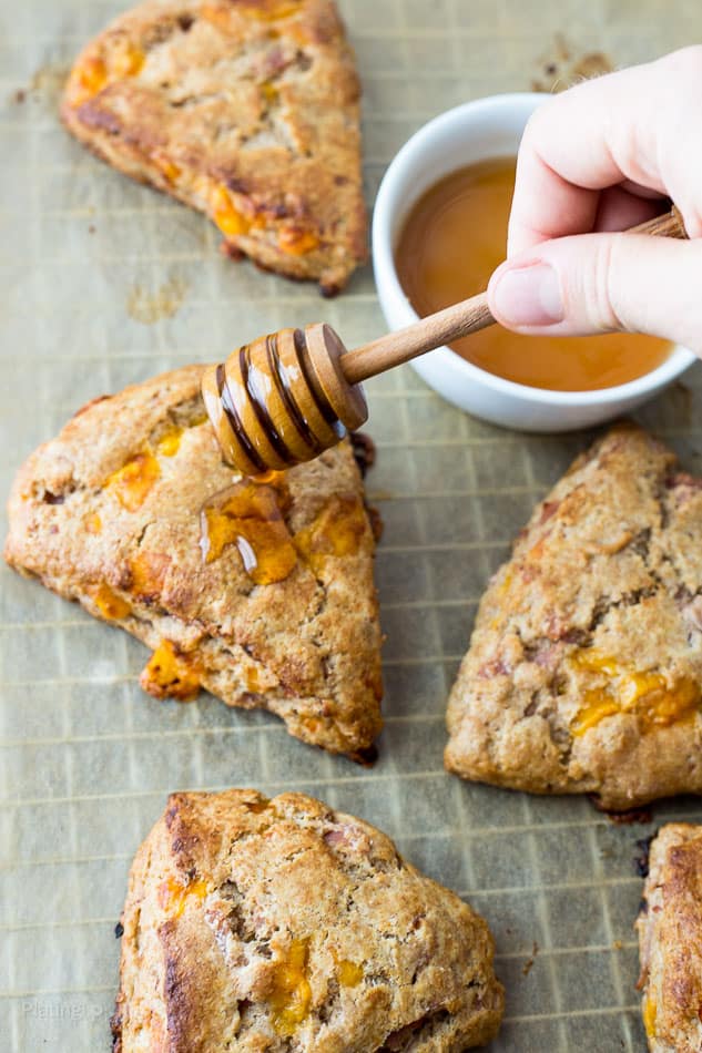 Whole wheat ham and cheddar savory scones on parchment paper with hand drizzling honey on one of them