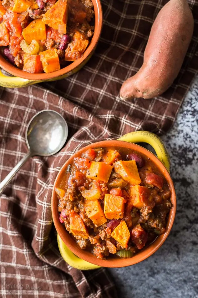 An overhead shot of roasted sweet potato chili in two small bowls with a spoon at the side