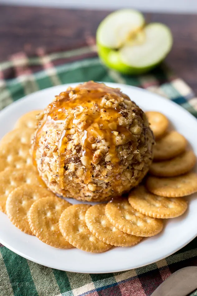 A Caramel Apple Cheese Ball on a plate with crackers around it and apple in background