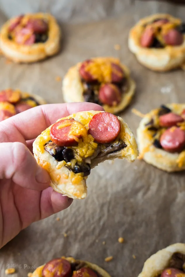 A hand holding Cheesy Hot Dog Tartlets with a bite out