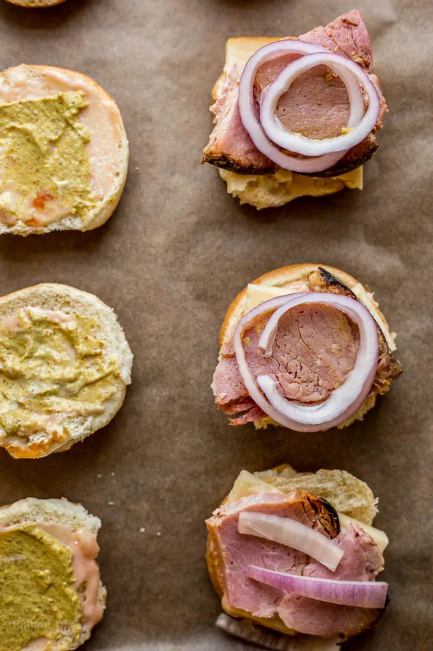 An overhead shot of open ham and gruyere sliders topped with onion and mustard