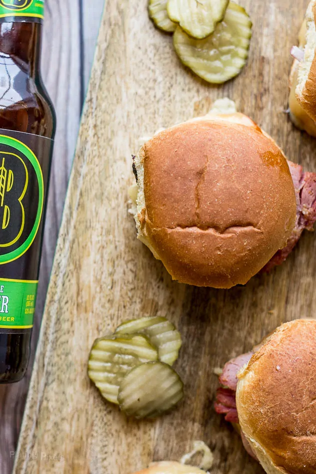 A close up of Ham and Gruyere Sliders on a wooden board with beer and pickles