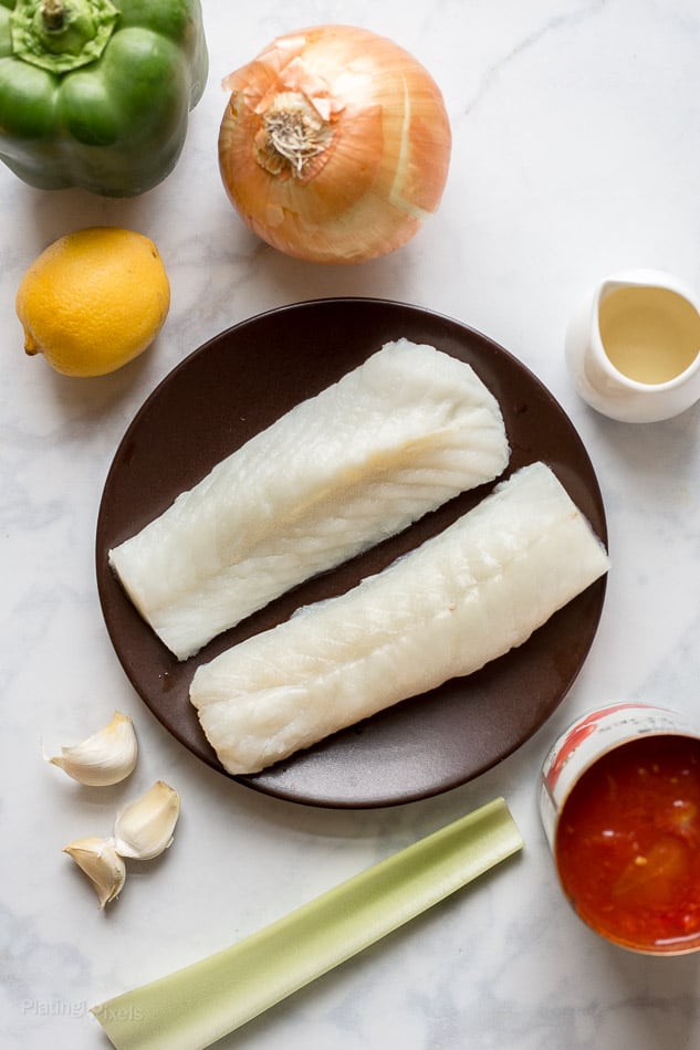 An overhead shot of two fillets of Cod and other ingredients to make a fish soup 