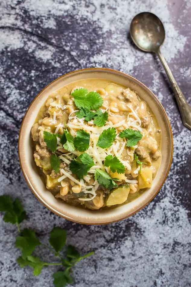 A bowl of White Bean Turkey Chili on a blue work surface with a spoon at the side